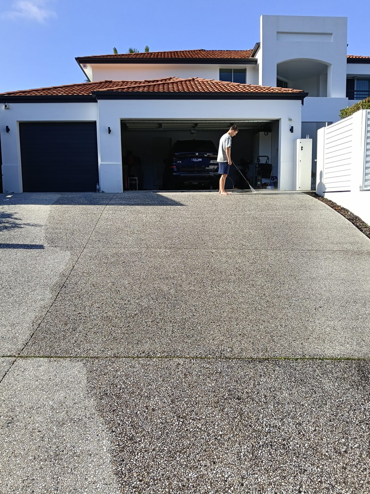 A double exposed-aggregate driveway in Noosa, with the cleaned left-hand strip much lighter than the untouched concrete beside it.