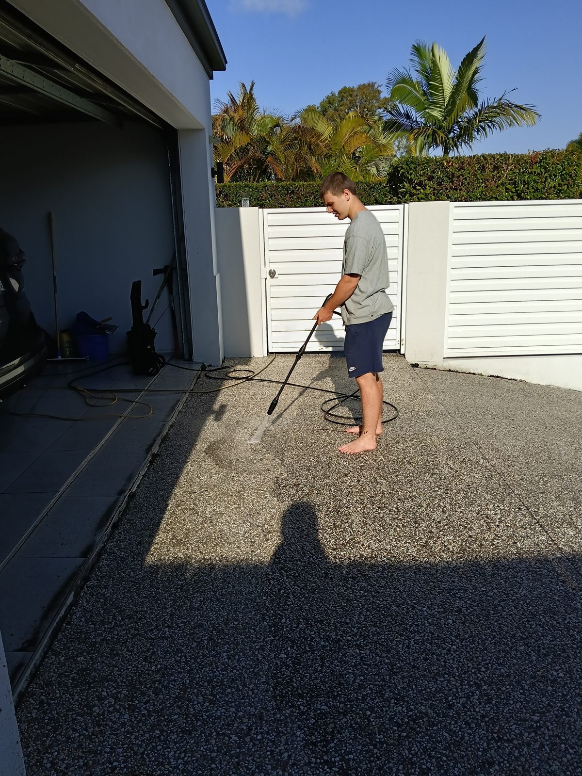 Ed pressure washing an exposed-aggregate side driveway by the gate.